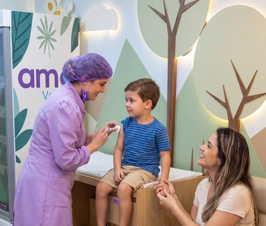Enfermeira da Amo Vacinas vacinando um menino com a mãe ao lado